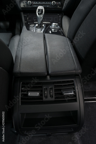 Modern car interior with luxury leather armrest and rear ventilation control panel.