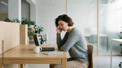 Tired Woman Rubbing Eyes At Her Desk In Modern Office Environment