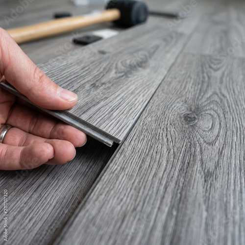 Close-up of hands installing grey laminate flooring with rubber mallet