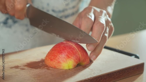 Woman’s hand slicing apple with kitchen knife on wooden cutting board