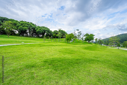 An expansive, lush green lawn set against rolling distant mountains under a blue sky with white clouds.