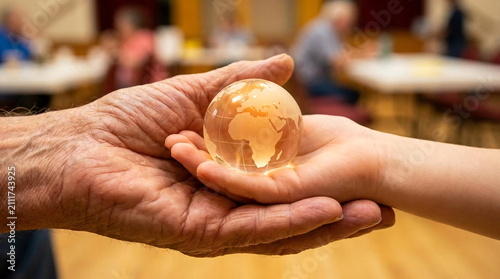 Elderly hands holding a small glass world globe.