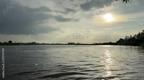 Dramatic sun shining over calm river water under cloudy sky. 4k video 60 fps