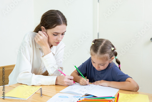 Teacher assisting young student with drawing and learning activity in classroom. Creative education, child development, personalized learning, and academic support concept.
