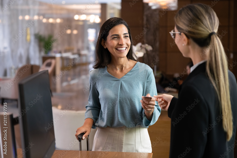 Naklejka premium Smiling Latina female, hotel guest finalizing check-in by receiving key card from receptionist at reception desk. Travel, customer satisfaction, luxury accommodation, hospitality services concept