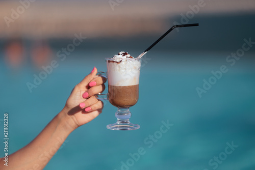 фотографія Woman Hand With Pink Manicure Holding Iced Coffee Near Pool