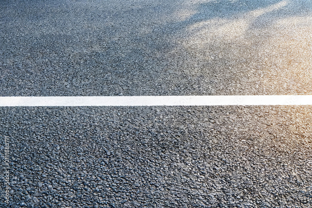 Fototapeta premium A close-up view of a dark asphalt road surface with a bright white lane marking, showing road texture.