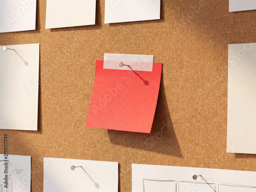 Red sticky note pinned on a brown cork board with many blank white papers