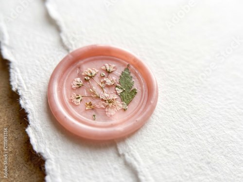 Pink wax seal with gold leaf decoration on a textured paper surface