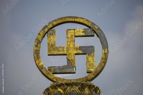 Golden swastika symbol in traditional Buddhist form, symbol of luck, protection and the cosmic order of Buddha's teaching, the circular bezel and lotus ornaments emphasize purity and spiritual perfection. Chee Chin Khor Temple, Bangkok, Thailand