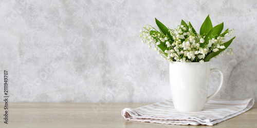Bouquet of lily of the valley flowers in a white ceramic mug on a wooden table