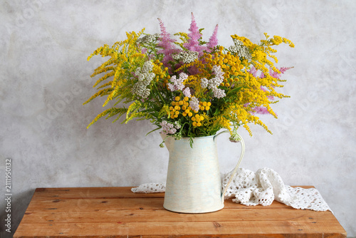 bouquet of flowers in a jug on the table: yarrow and astilbe, goldenrod and tansy. Summer still life, cottage decor and interior concept.