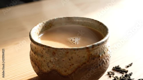 Rustic ceramic mug with milk tea and loose leaves on wood