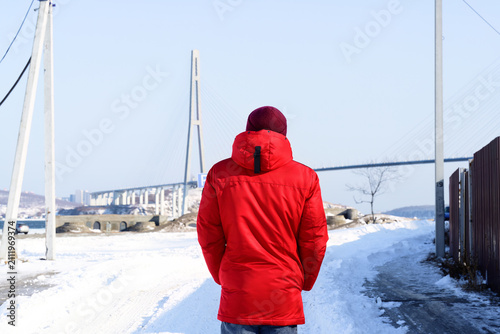 Bild auf Leinwand Russian man 30 years old standing with back view and looking at Russky Bridge in Vladivostok in winter, road to Russky Island, Sea of Japan
