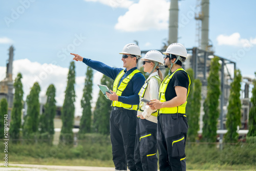 Three construction workers in safety gear discussing project plans at industrial site under blue sky