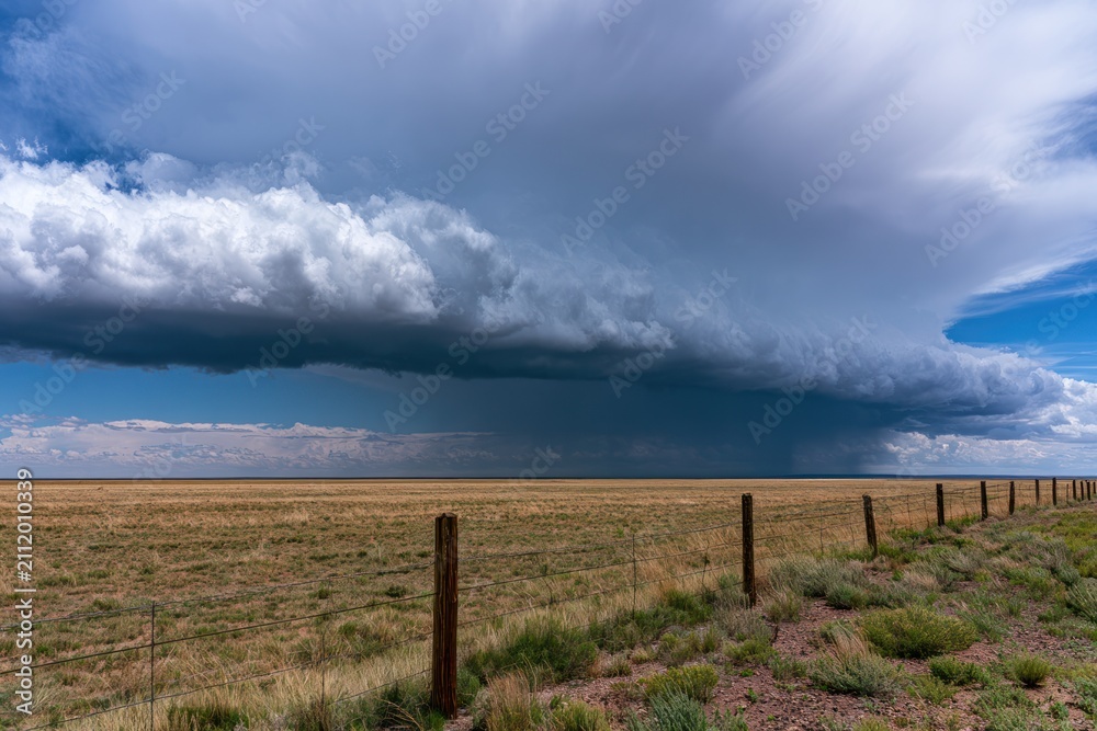 Fototapeta premium Expansive prairie landscape with dramatic storm clouds and wooden fence under blue sky