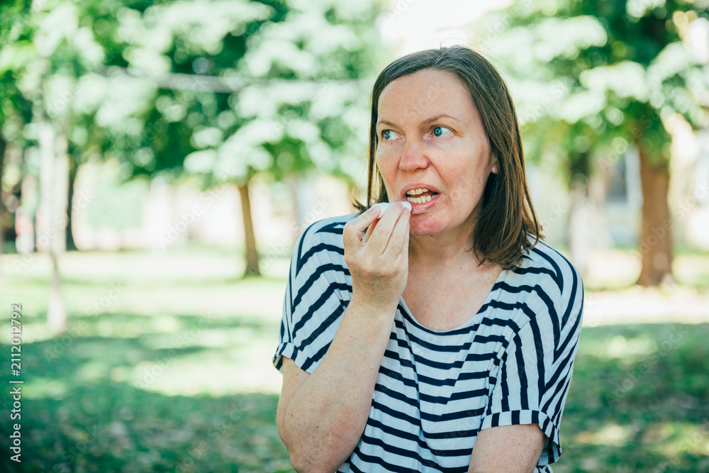 Fototapeta premium Middle-aged woman applying lip balm while sitting in a sunny city park. Self-care, skincare, personal wellness and healthy outdoor lifestyle concept.