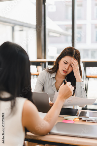 Stressed Asian businesswoman holding document while working with colleague in office