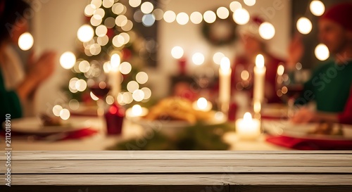 Empty wooden table top with blurred christmas dinner party background with festive lights, candles, and people celebrating in a cozy home setting