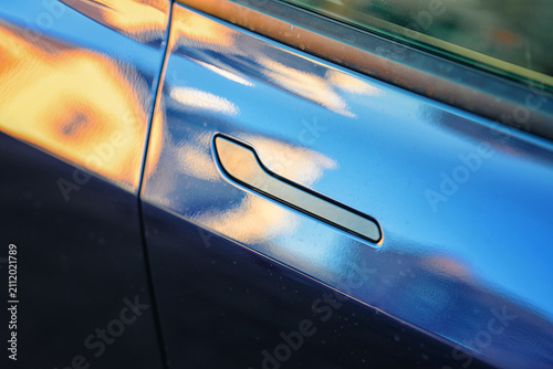 Retractable flush door handle seamlessly integrated into the glossy blue metallic body panel of modern luxury electric automobile. Flush door handle on blue metallic car. Selective focus