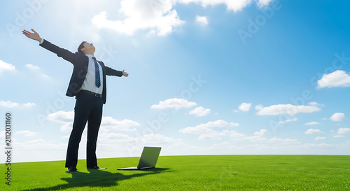 Businessman celebrating success with arms outstretched in a sunny green field, laptop nearby, bright blue sky with clouds, freedom, achievement, modern work.
