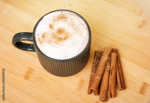 Cup of cappuccino with cinnamon sticks on wooden plate. Cozy warm drink, inviting, comfort mood