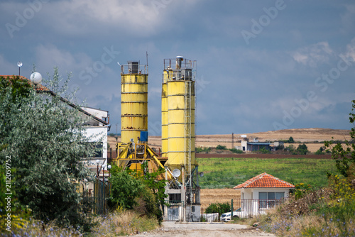 Fotografie two tall, weathered yellow industrial silos dominate the landscape at the end of a dirt access road