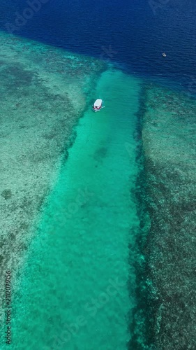 Boat floating, in tropical reef, with boat, reef, from a aerial view perspective, with blue, green accents, and relaxing holiday mood, showing nearby objects and surrounding setting.