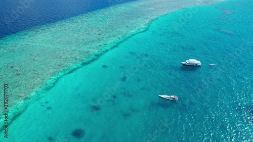 Aerial view of a boat gently floating on tranquil tropical waters in the Maldives, surrounded by sandy reefs and vibrant blue-green hues, creating a serene and relaxing holiday travel id.