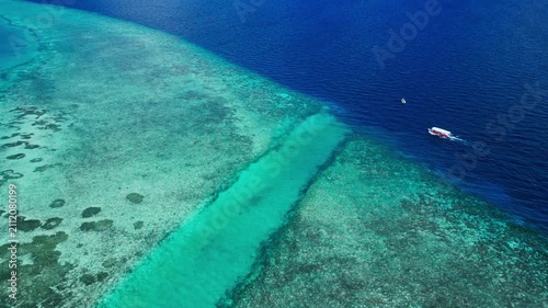 A serene and tranquil aerial view of a boat on vibrant tropical reefs in the Maldives, captured from a high-altitude perspective. The scene showcases the beauty of the transparent water.