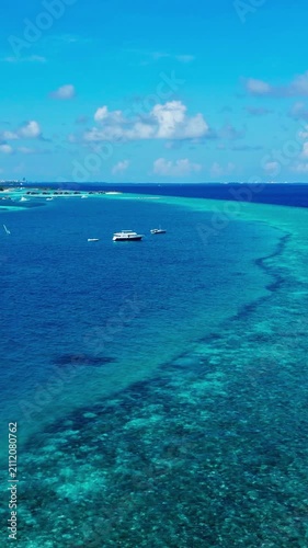 Boat floating, in tropical reef, with boat, reef, from a aerial view perspective, with blue, green accents, and relaxed serene mood, showing nearby objects and surrounding setting, vertical video