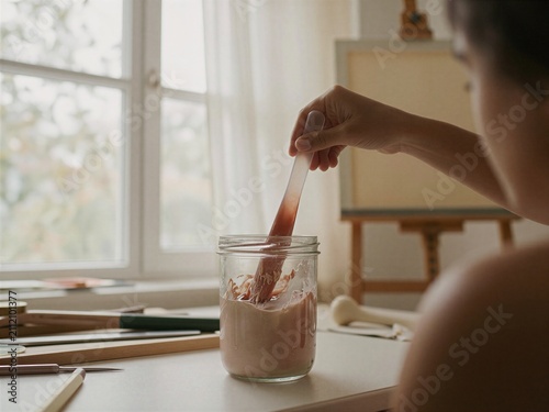 Hand stirring ceramic glaze in jar at bright artist studio
