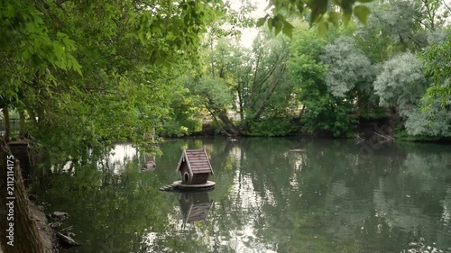 Peaceful pond with floating birdhouses surrounded by lush green trees and reflective water