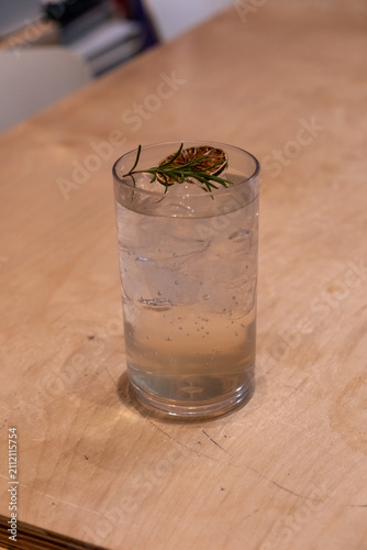 Iced sparkling drink served in a glass, with rosemary and dried citrus slice on a wooden table.