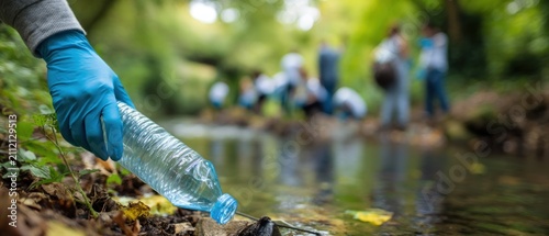 Person in blue glove removing plastic bottle from stream people cleaning in background