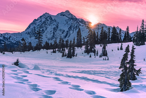 Cuadro en lienzo Golden winter sunset glows behind a snow covered mountain as sunlight breaks ove