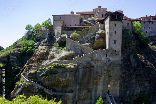 Fotografie Tourists ascend the stone steps to the Great Meteoron Monastery, perched atop a rock formation in Meteora, Greece, on a sunny day