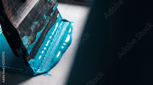 Close up view of screen printing process with vibrant blue ink being spread across a mesh screen.