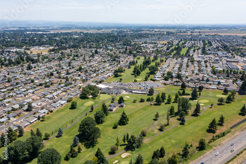 Aerial drone photo of Woodburn, Oregon, USA featuring residential neighborhoods, green parks, golf course, and surrounding Willamette Valley landscape on a clear summer day