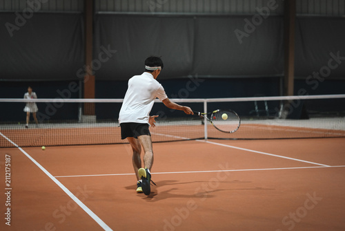 Fotografie Male Tennis Player Hitting Forehand Shot on Indoor Clay Court During Match
