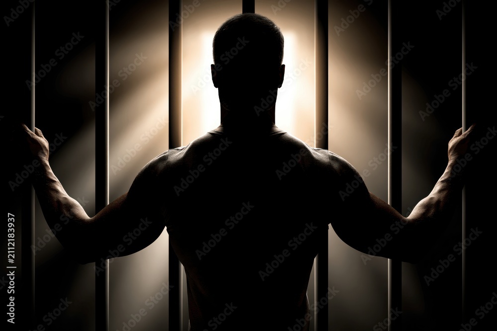 Obraz premium Man in Silhouette Behind Prison Bars Reaching Towards Light