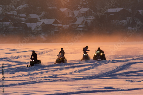 Fotografie Group of friends riding snowmobiles across a vast frozen field during a scenic g