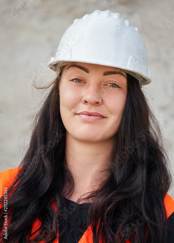 Young female construction worker with hard hat helmet and bright orange vest, closeup portrait