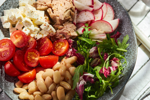Healthy Mediterranean salad with canned tuna, white beans, feta cheese, cherry tomatoes, and greens on a stone plate.