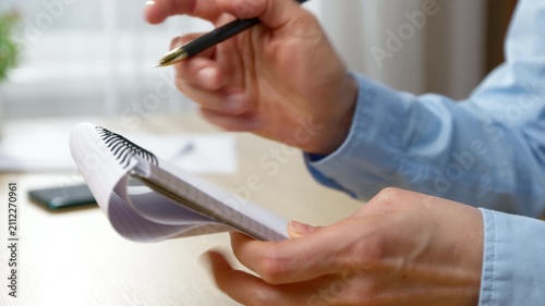 Person writing notes in spiral paper pad with pen. Hand taking information during business planning process.