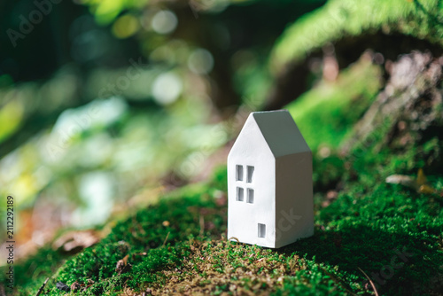 Concept of business in real estate, mortgage, rent. Miniature white house with moss and blurred leaves on background.