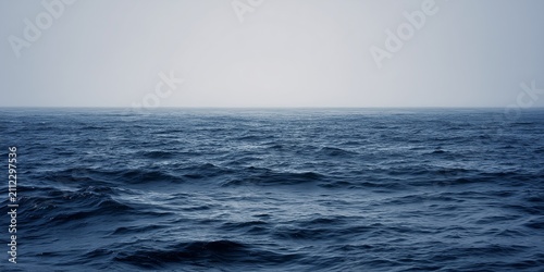 Calm deep blue ocean water surface under foggy mist sky background with soft calm waves on horizon, minimal seascape