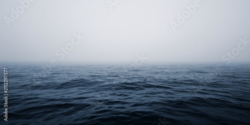 Vast open deep blue ocean water waves surface beneath overcast misty sky at calm sea horizon, minimal seascape