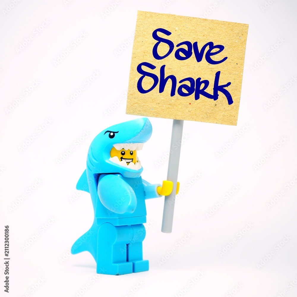 Fototapeta premium Indonesia - October 4, 2025 : Mini toy of action figure at table with blurred background. Miniature photography concept design. Minifigure of Shark guy character hold SAVE ME poster banner campaign