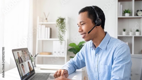 Indonesian business man speaking having virtual meeting on laptop. Wearing headset talking consulting on video call at home office call center.